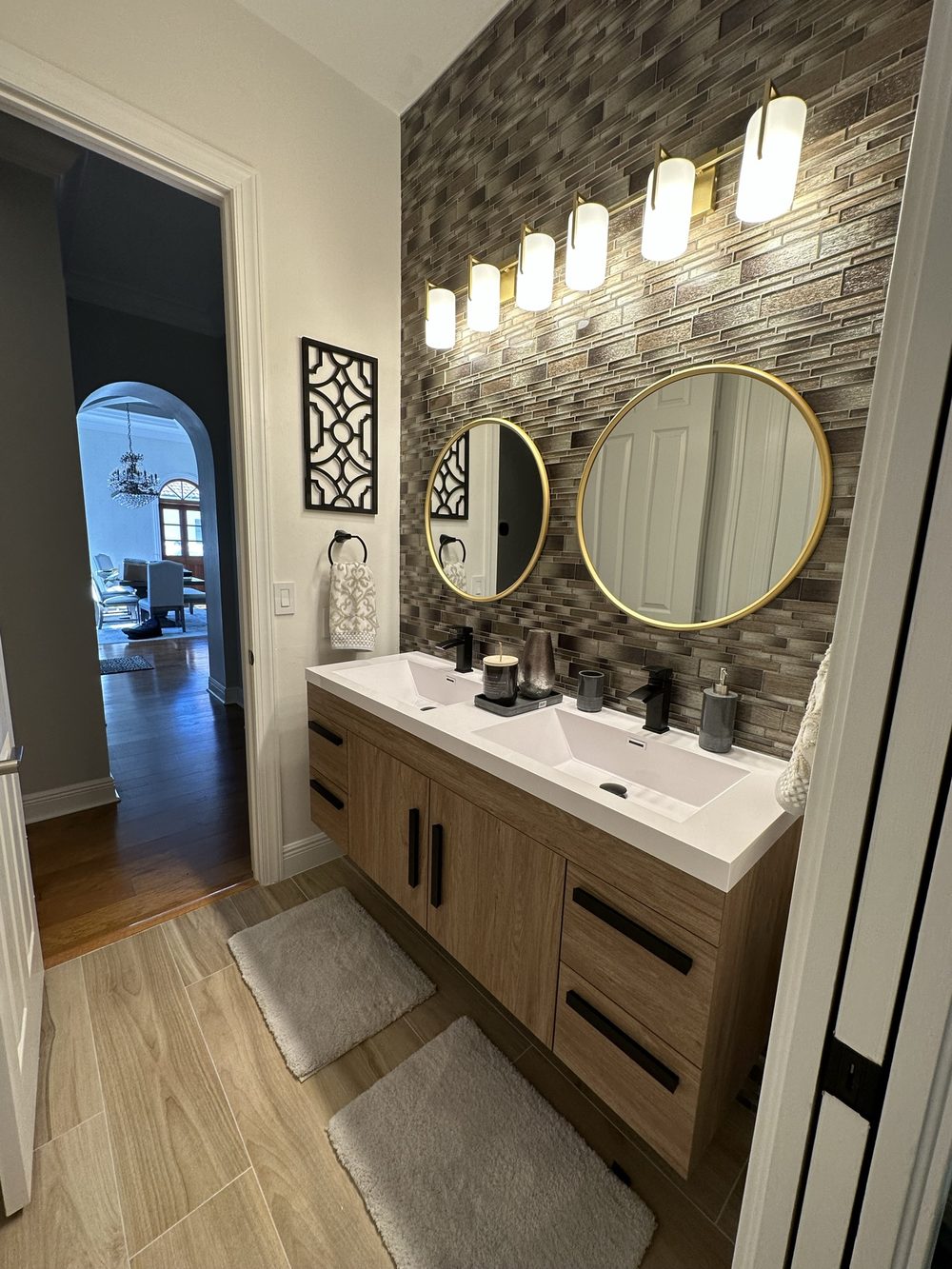 Guest bathroom after remodel — modern floating vanity with round gold mirrors and stone accent wall