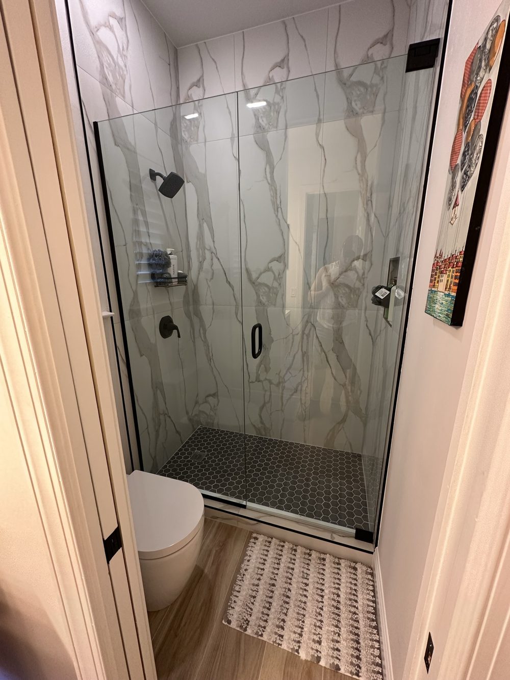 Shower after remodel — frameless glass walk-in shower with marble-look porcelain slab walls and black hexagon tile floor