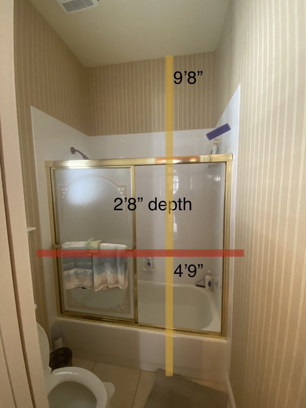 Shower before remodel — dated gold-framed sliding glass door over tub with striped wallpaper