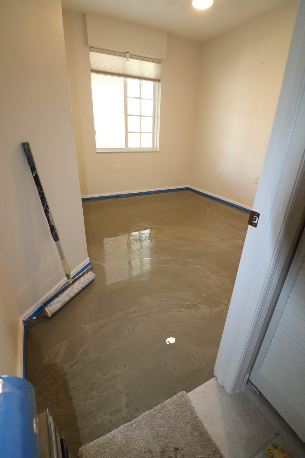 Room before LVP flooring installation — bare wet concrete subfloor with baseboard taped off